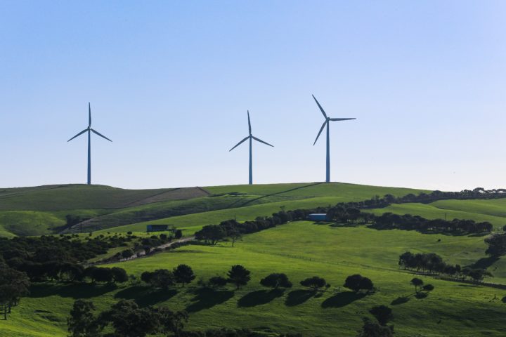 Three wind turbines on top of a green hill.
